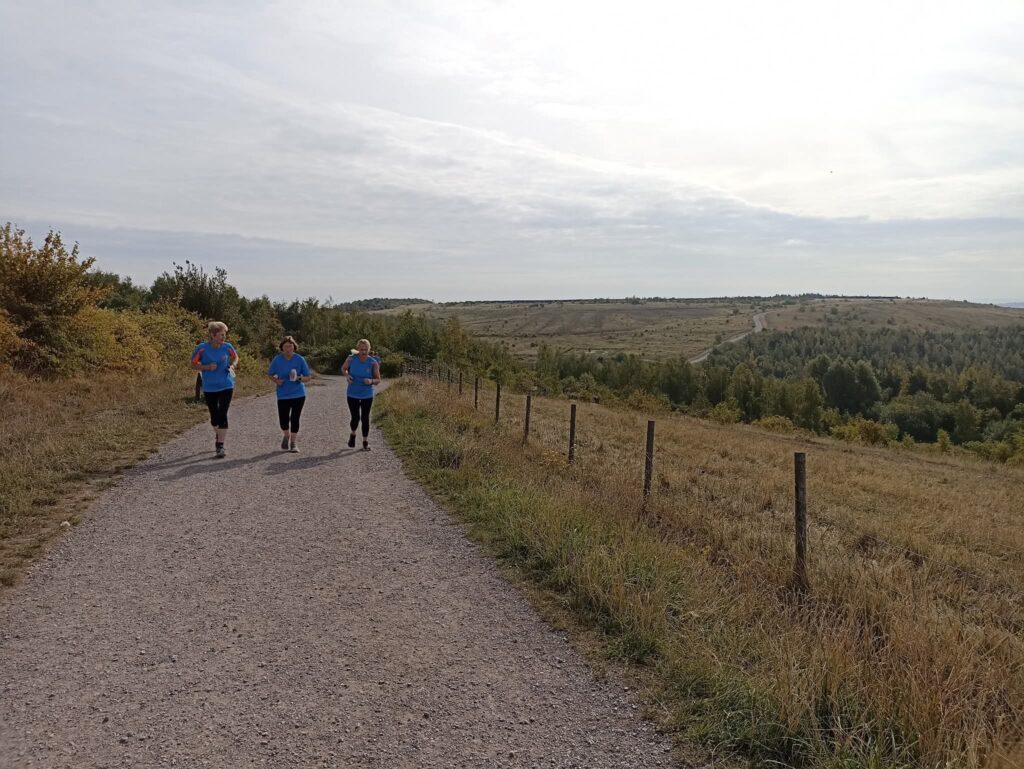 Three runners on a path amongst open green hills